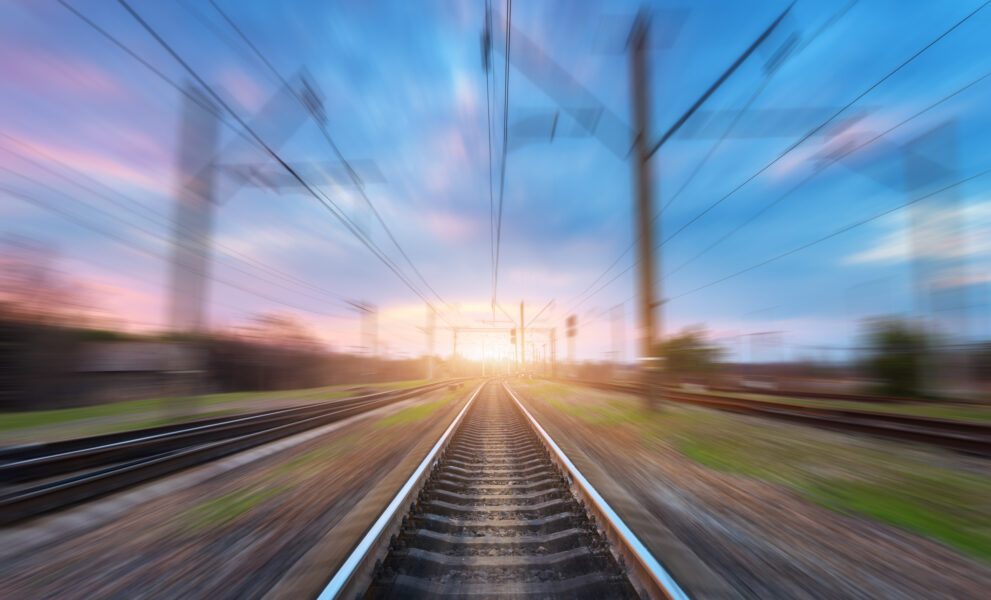 railway-station-with-motion-blur-effect-at-sunset-blurred-railroad-industrial-conceptual-landscape-with-blurred-railway-station-blue-sky-with-colorful-clouds-and-sunlight-railway-track-background